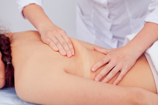 массажист делает антицеллюлитный массаж женской спины в салоне красоты